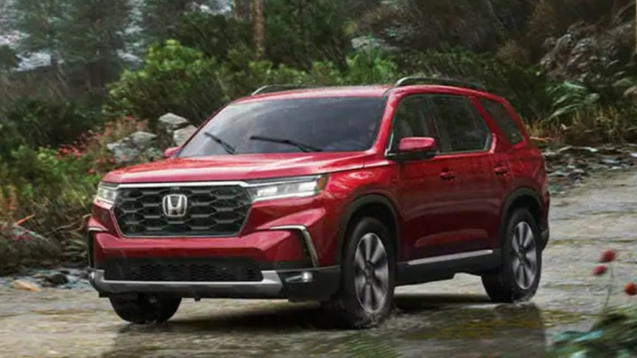 A red 2023 Honda Pilot midsize SUV is driving off-road.