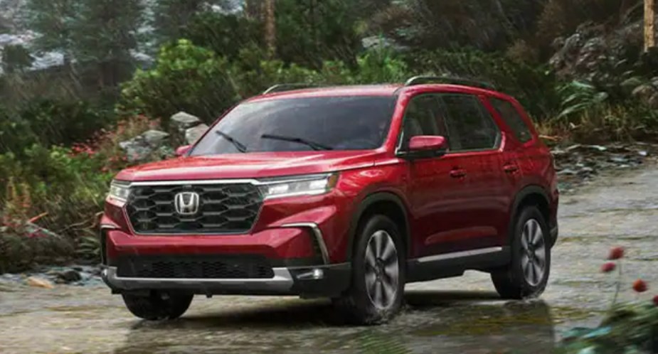 A red 2023 Honda Pilot midsize SUV is driving off-road. 