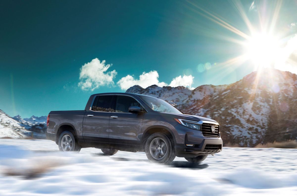 A dark gray 2023 model Honda Ridgeline midsize pickup truck driving on snow as the sun shines on a hill