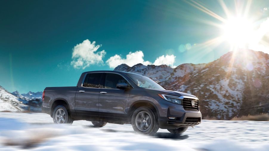 A dark-gray 2023 Honda Ridgeline midsize pickup truck model driving over snow as the sun shines over a hill