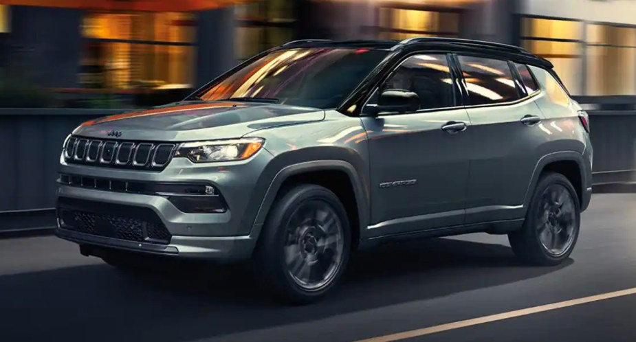 A gray 2023 Jeep Compass small SUV is driving on the road. 