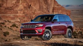 A red 2023 Jeep Grand Cherokee Summit Reserve midsize SUV model parked on rocky terrain in a desert near red cliffs