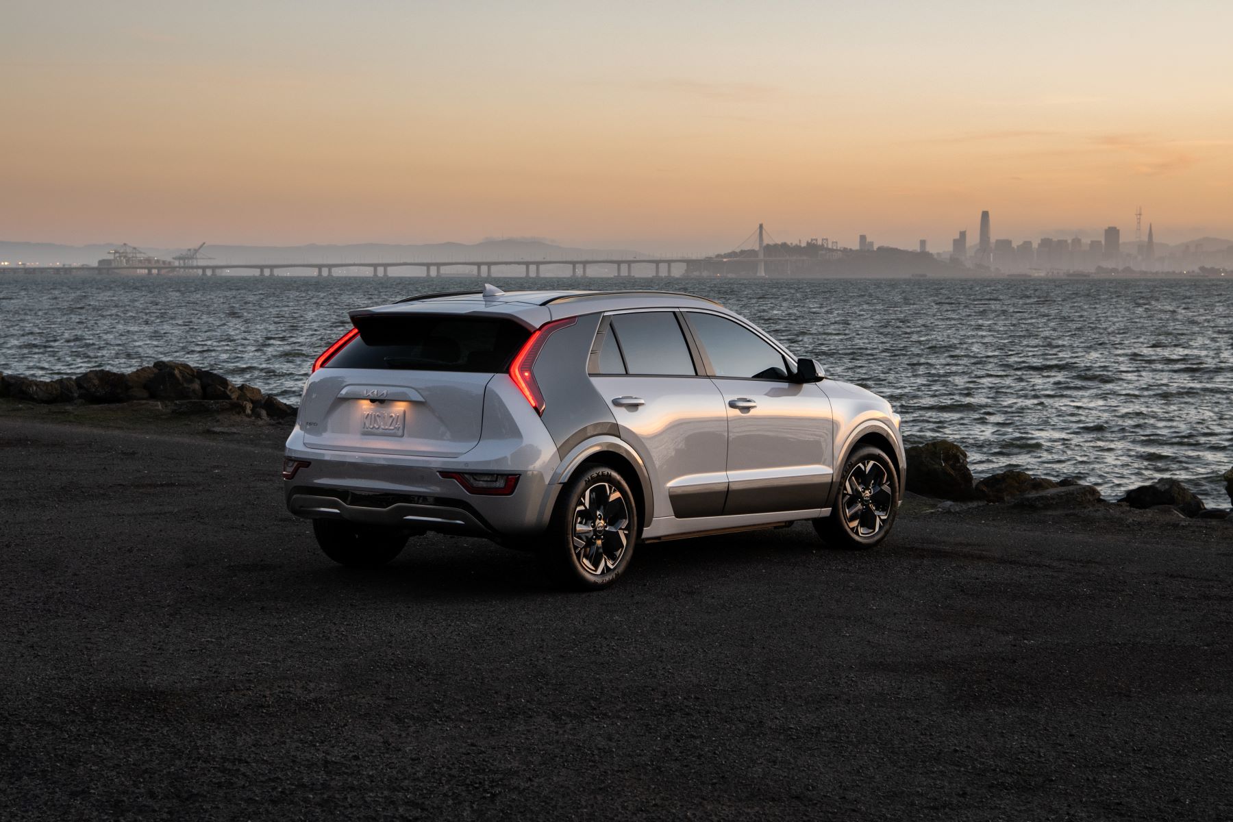 A 2023 Kia Niro EV compact electric SUV model parked a beach overlooking a city skyline at dusk