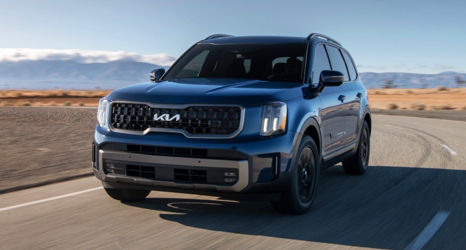 A blue 2023 Kia Telluride midsize SUV is driving on the road. 