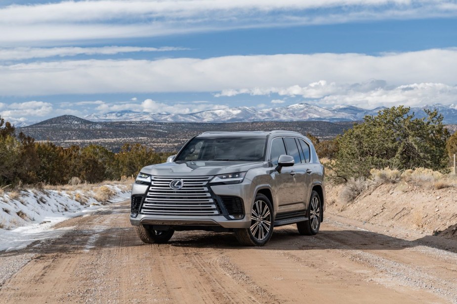 A silver Lexus LX 600 SUV parked on a snowy dirt road, a mountain range visible in the background.