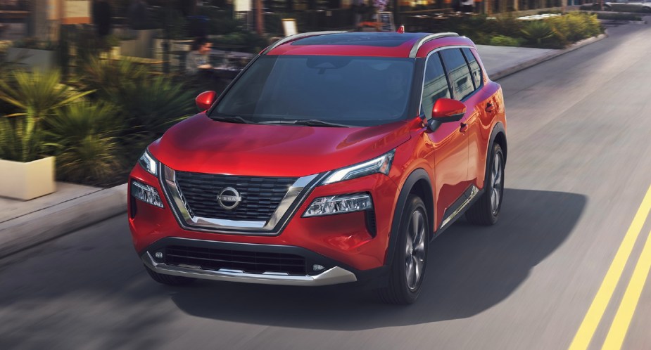 A red 2023 Nissan Rogue small SUV is driving on the road.
