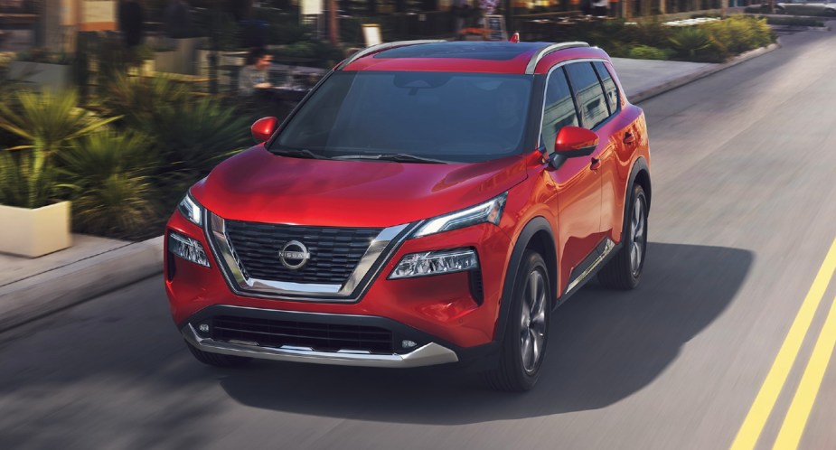A red 2023 Nissan Rogue small SUV is driving on the road. 