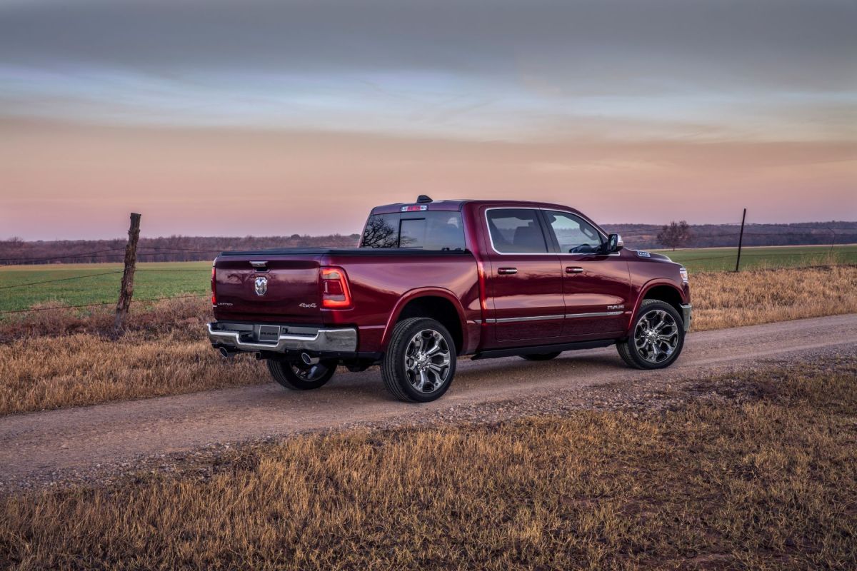 A red 2023 Ram 1500 Limited model full-size pickup truck parked on a gravel driveway near farmland