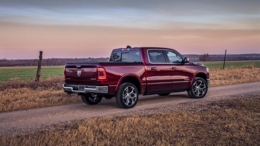 A red 2023 Ram 1500 Limited full-size pickup truck model parked on a dirt gravel trail near farmland