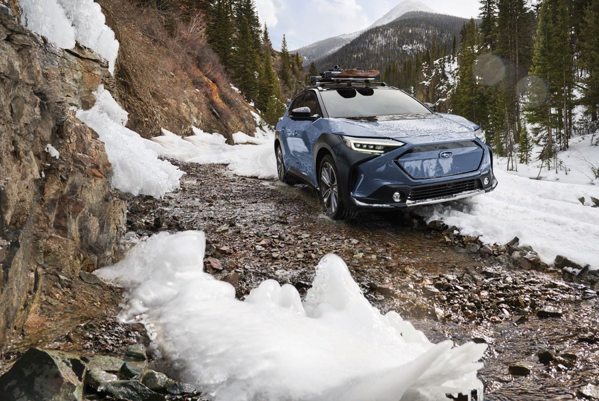 A blue 2023 Subaru Solterra electric SUV with AWD off-road driving in the mountains over rocks and snow