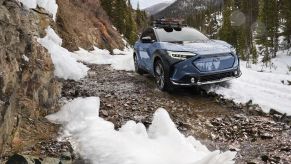 A blue 2023 Subaru Solterra electric SUV with AWD off-road driving in the mountains over rocks and snow