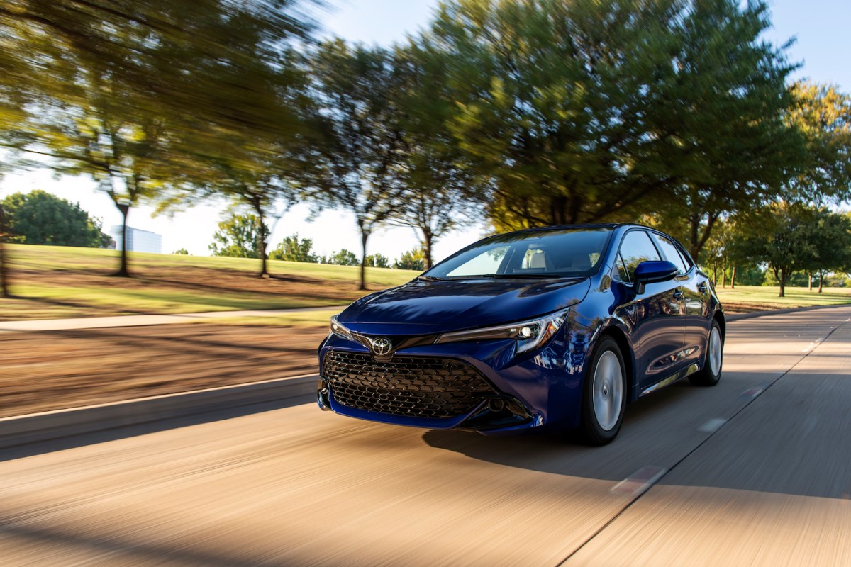 A 2023 Toyota Corolla Hatchback in metallic blue driving down a tree-lined street