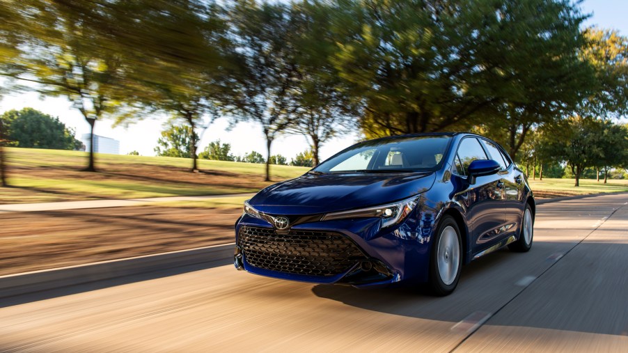 A 2023 Toyota Corolla Hatchback in metallic blue driving down a tree-lined street