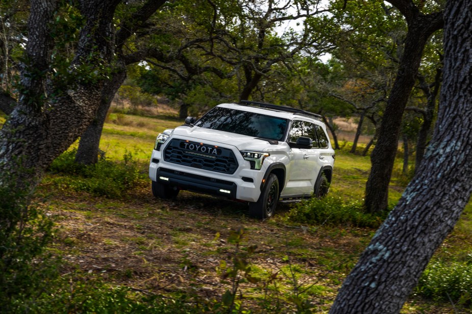 A white 2023 Toyota Sequoia TRD Pro SUV parked on a 4WD trail, amongst a stand of pine trees.