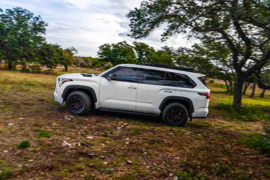 A white 2023 Toyota Sequoia TRD Pro speeds down an off-road trail with a line of trees visible in the background.