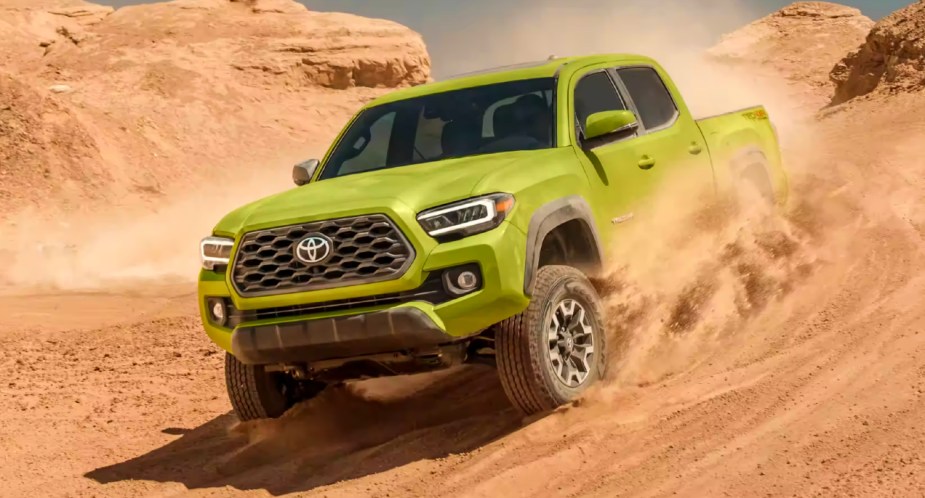 A green 2023 Toyota Tacoma midsize pickup truck is driving off-road on sand. 