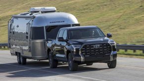 Publicity photo of a 2023 Toyota Tundra pulling an Airstream travel trailer up a highway, a green hillside visible in the background.