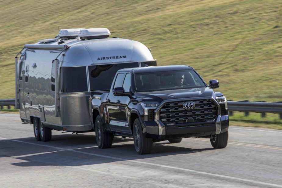 Publicity photo of a 2023 Toyota Tundra pulling an Airstream travel trailer down a highway, with a green hillside visible in the background.