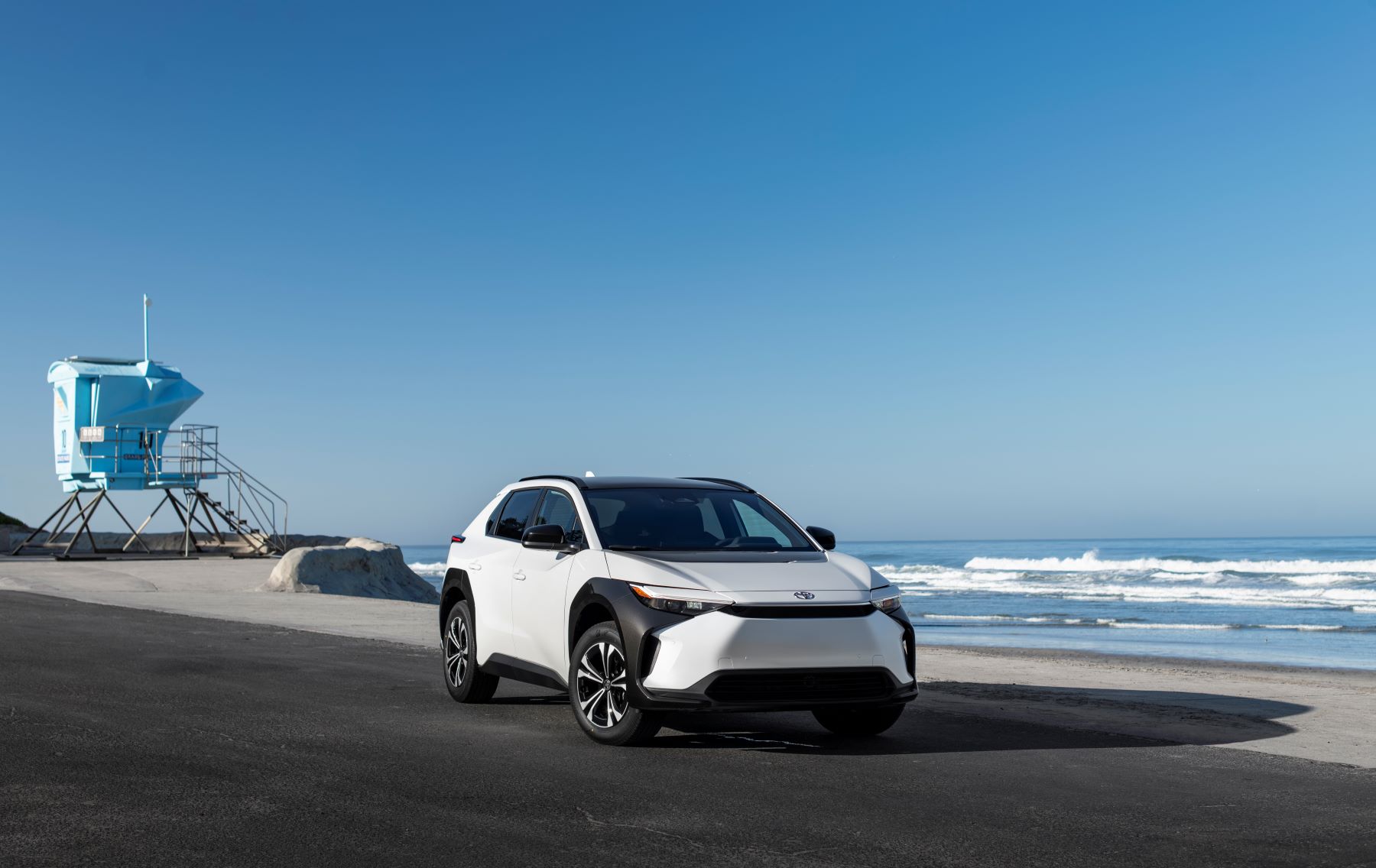 A 2023 Toyota bz4X compact electric SUV model in Wind Chill Pearl is parked on a beach near a lifeguard station.