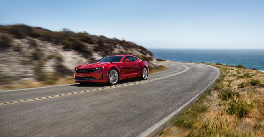 The 2022 Chevy Camaro LT1 V6, like this red one cornering on a coastal road, is one of the most affordable sports cars.