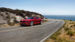 The 2022 Chevy Camaro LT1 V6, like this red one cornering on a coastal road, is one of the most affordable sports cars.