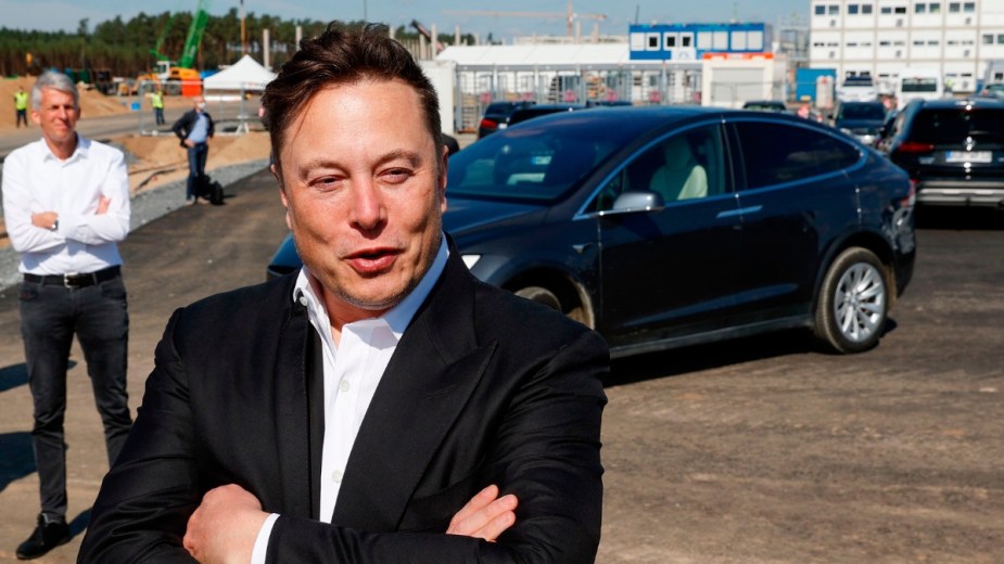 Elon Musk standing in front of a Model Y electric crossover SUV, highlighting how he got the name Tesla