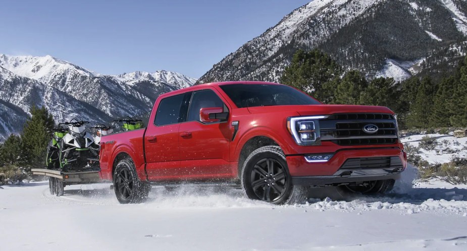 A red 2023 Ford F-150 full-size pickup is driving in snow. 