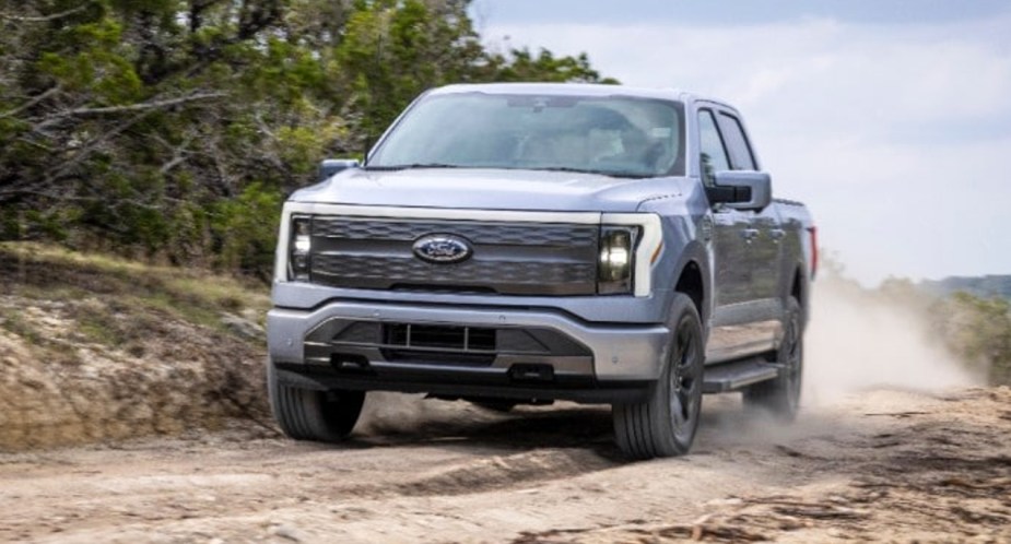 A gray 2023 Ford F-150 Lightning electric pickup truck is driving off-road. 