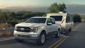 A white 2023 Ford F-150 full-size pickup truck is driving on the road towing a trailer.