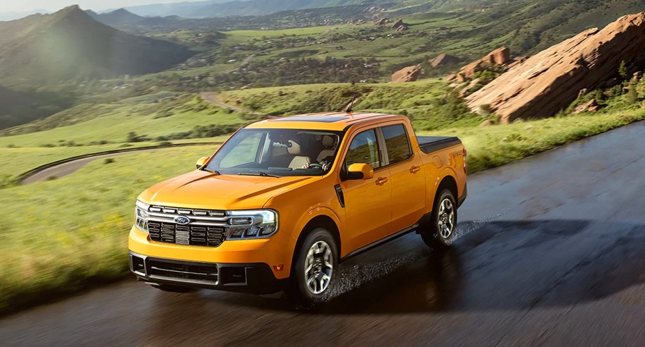 A yellow 2023 Ford Maverick small pickup truck is driving on a wet road. 