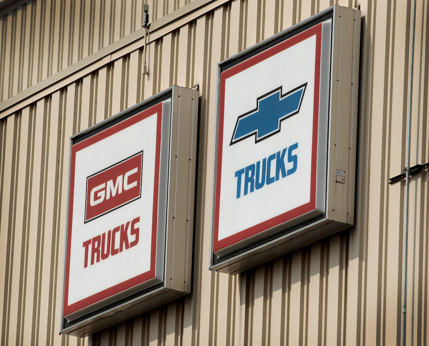 Vintage signs for GMC trucks and Chevy pickup trucks hanging on a tan, metal wall.