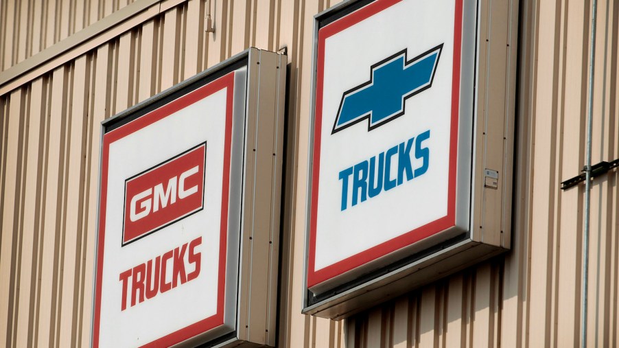 Vintage signs for GMC trucks and Chevy pickup trucks hanging on a tan, metal wall.