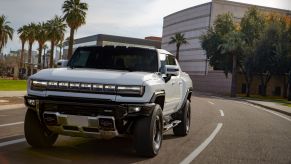 A white GMC Hummer EV electric pickup truck driving past palm trees