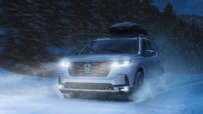 A white 2023 Honda Pilot midsize SUV is driving through the snow.
