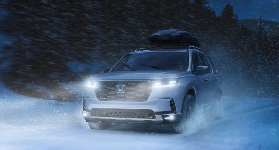 A white 2023 Honda Pilot midsize SUV is driving in the snow. 