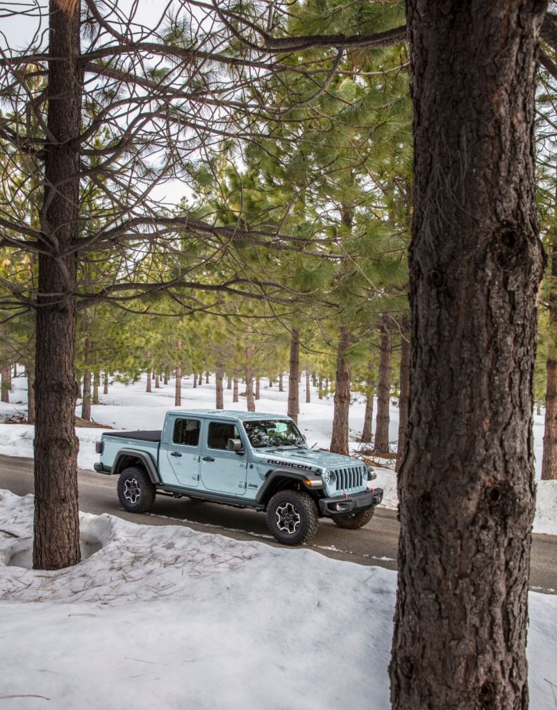 A 2023 Jeep Gladiator in the new Jeep color, early gray paint, driving through the woods.