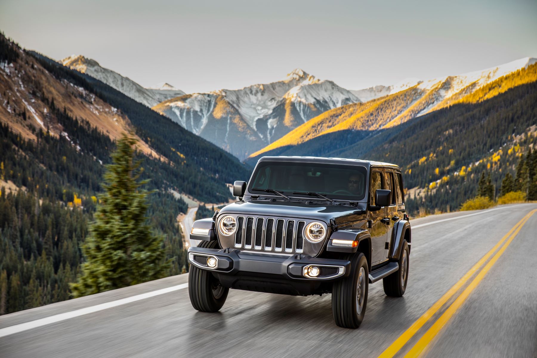 A dark gray Jeep Wrangler Unlimited off-road SUV model driving on a highway near mountains