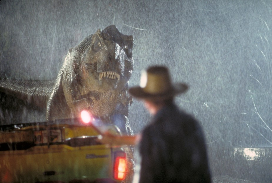 A T-Rex crushing a Jeep during the movie Jurassic Park, an actor visible in the foreground.