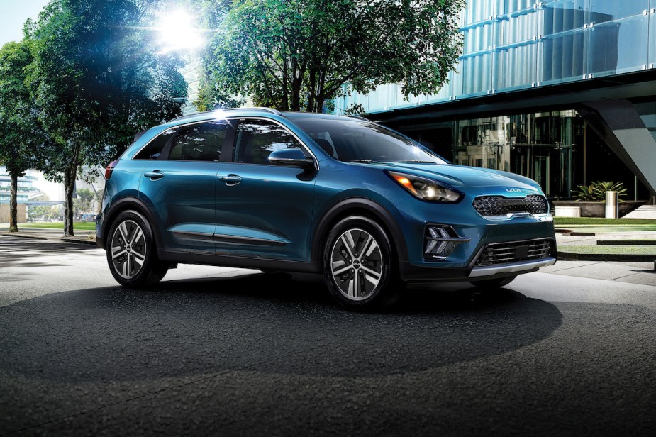 A blue Kia Niro PHEV parked outdoors in front of a large building. 