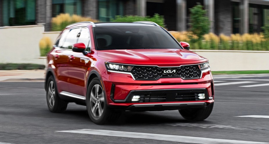A red Kia Sorento Hybrid mid-size hybrid SUV is driving on the highway. 