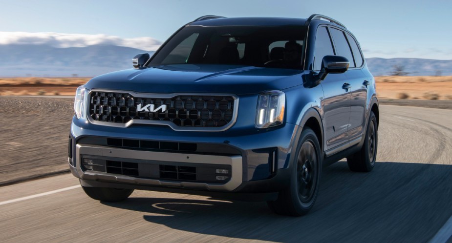 A blue 2023 Kia Telluride midsize SUV is driving on the road. 