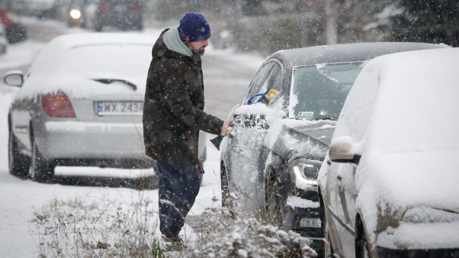 A man clears snow from his car, emphasizing that the Washington Post says not to heat the car before driving in the winter