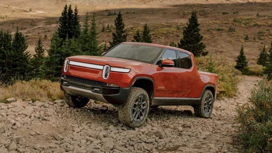 Orange 2023 Rivian R1T electric pickup truck driving up a hill