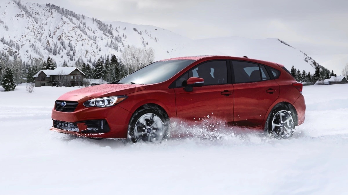 Red 2023 Subaru Impreza, the cheapest new Subaru car and most affordable AWD vehicle, driving in the snow