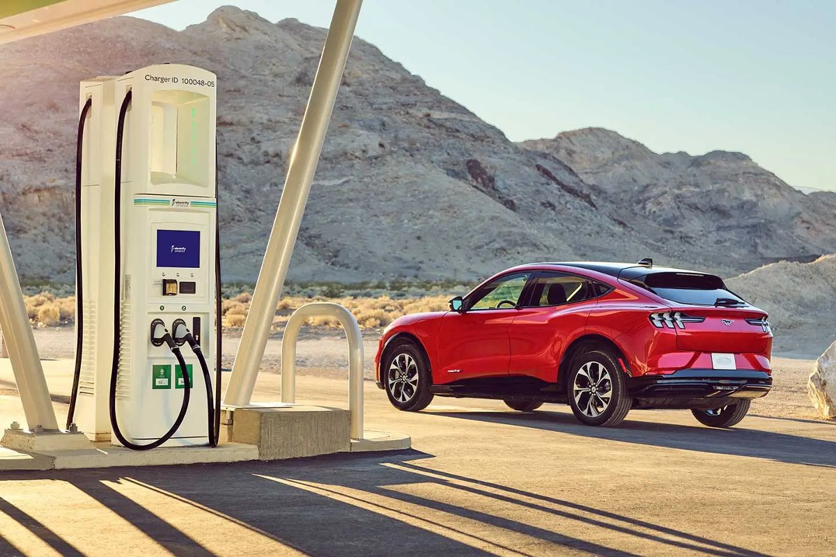 Red Ford Mustang Mach-E SUV by charging station, highlighting how EVs reduce gas consumption in America less than expected