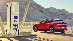 Red Ford Mustang Mach-E by charging station, highlighting how EVs reduce gas consumption in America less than expected