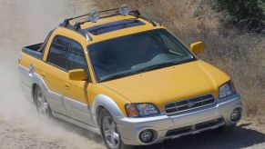 A yellow Subaru Baja compact utility pickup truck built with a midgate driving on a dusty gravel road