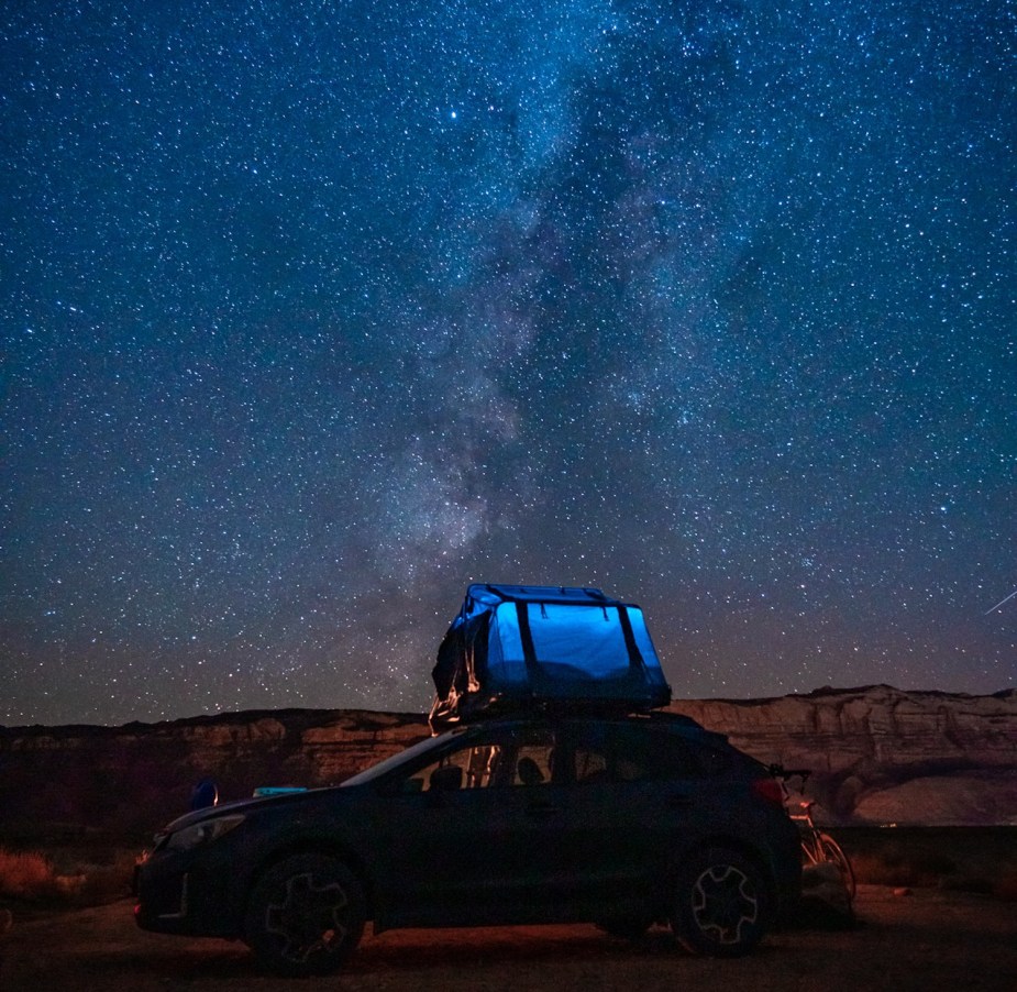 Promo photo of a Subaru car parked in a field beneath a bright night sky full of stars.