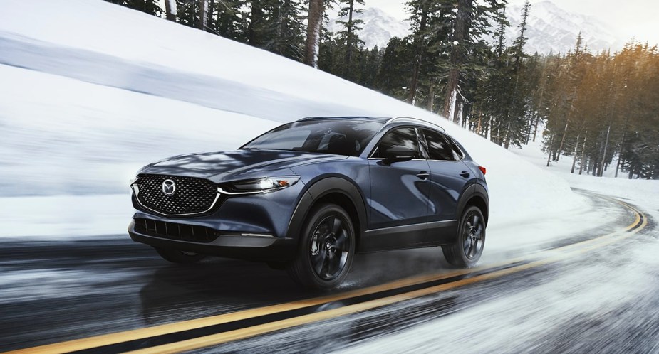 A blue Mazda CX-30 subcompact SUV is driving on a wet road. 