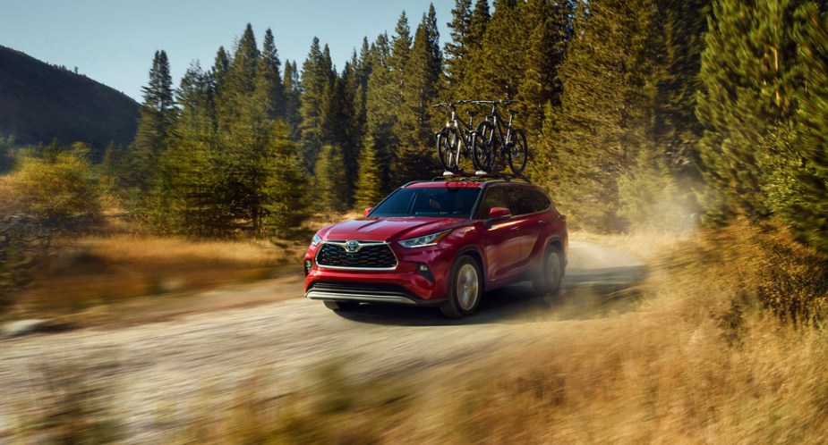 A red 2023 Toyota Highlander Hybrid midsize hybrid SUV is driving off-road. 